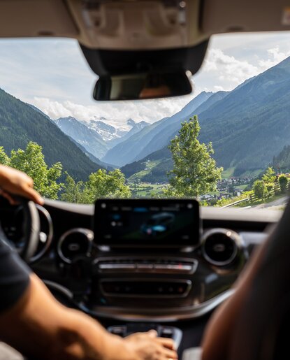 Blick aus Auto auf Berglandschaft mit grünen Bäumen und schneebedeckten Gipfeln