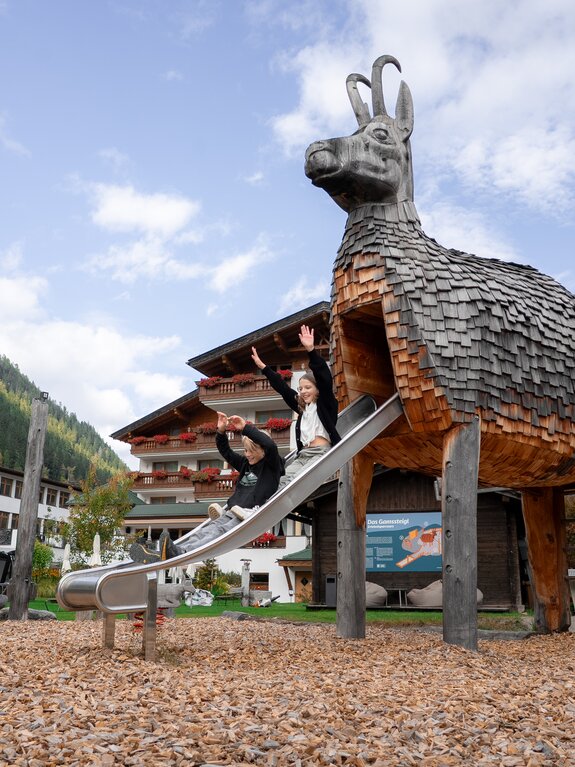 Lachende Kinder auf einer Rutsche, die wie eine Gämse aus Holz gebaut ist