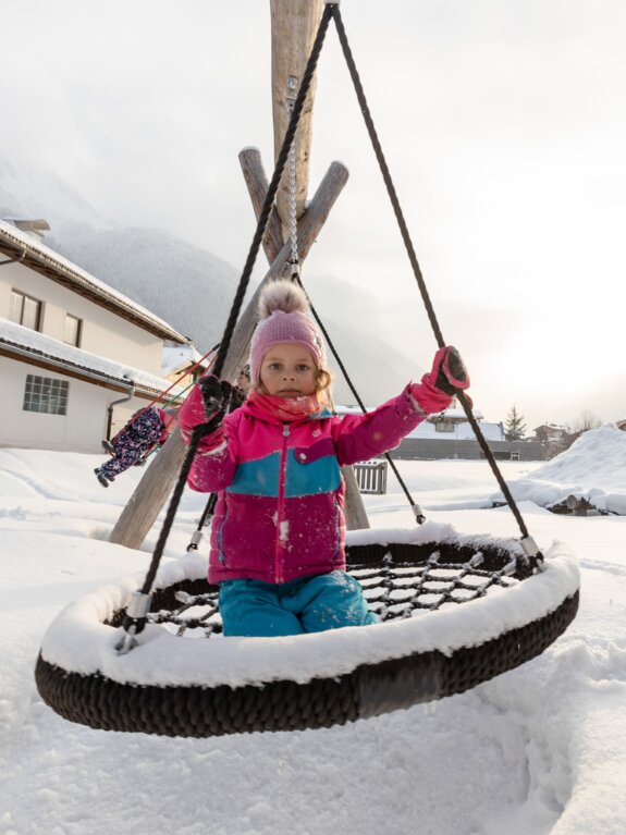 Mädchen sitzt auf einer schneebedeckten Nestschaukel im Winter