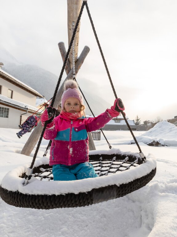 Mädchen sitzt auf einer schneebedeckten Nestschaukel im Winter