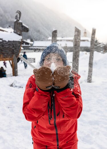 Kind mit Fäustlingen und roter Jacke pustet Schnee in die Luft