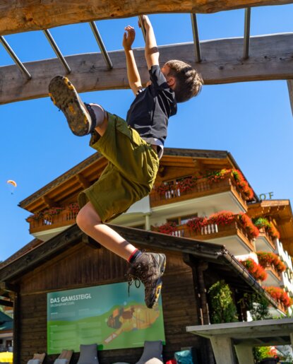 Junge hangelt an Klettergerüst vor Gebäude mit Blumenkästen