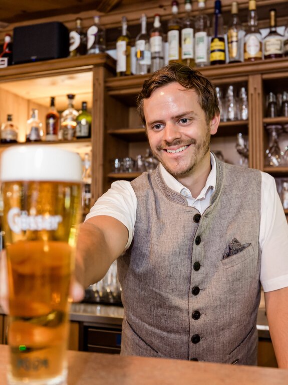 Gastgeber Andreas  reicht ein Glas Bier über eine Theke mit Spirituosenflaschen