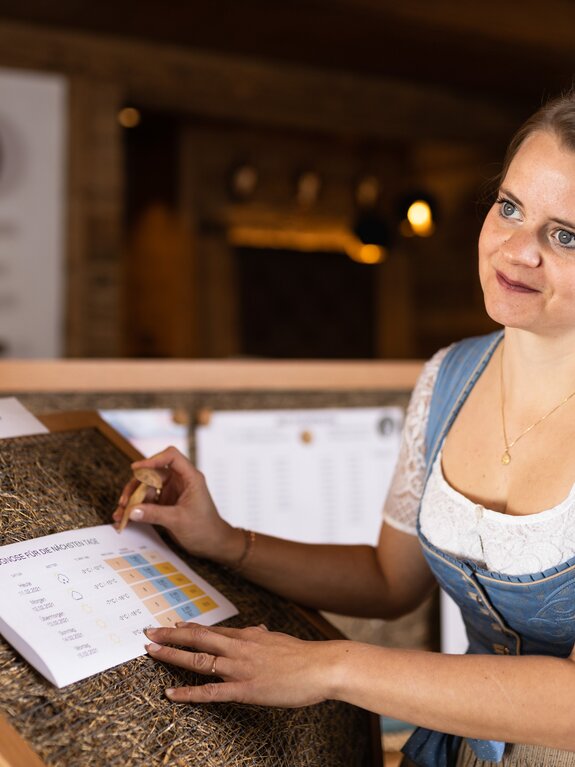 Martina im Dirndl erklärt Bergwetter an einer Infotafel