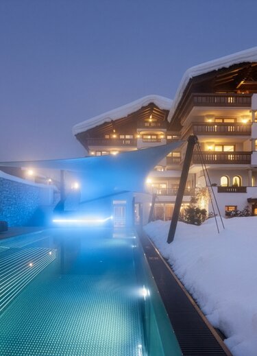 Beleuchteter Außenpool vor schneebedecktem Stubaierhof Hotel
