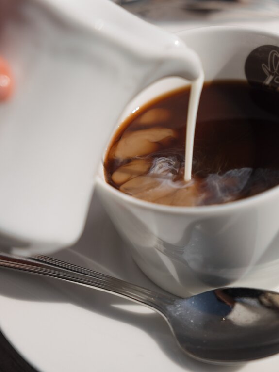 Milch wird in eine Tasse Kaffee gegossen