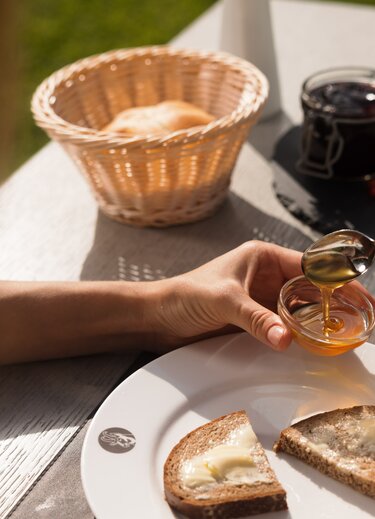 Frühstückstisch mit Brot, Honig, Marmelade und Brötchenkorb im Freien