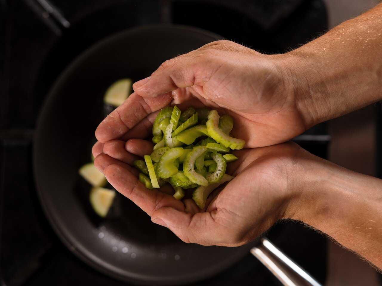 Hands holding sliced celery over a frying pan