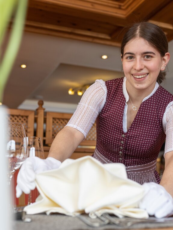 Frau im Dirndl deckt einen Tisch mit weißen Handschuhen