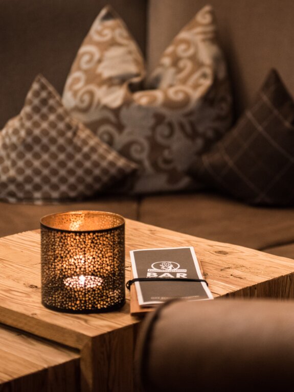 Kerze, Bar-Karte und Kissen auf einem Holztisch vor einem Sofa