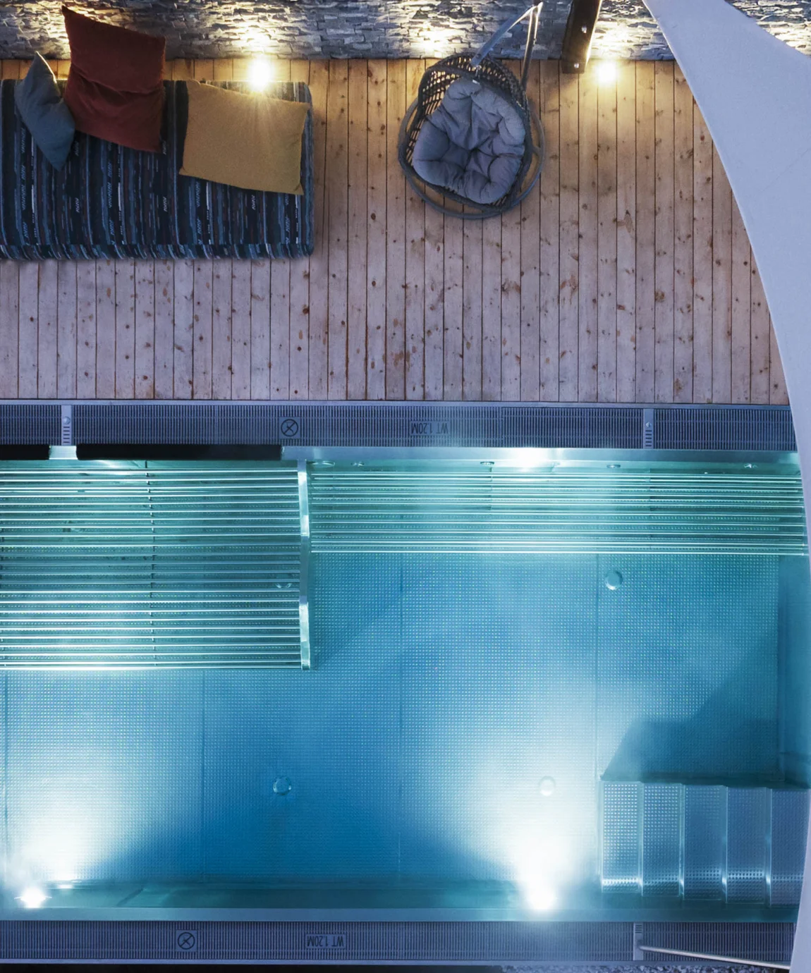 Draufsicht auf Pool mit Holzterrasse, Liegefläche und Sonnensegel bei Nacht