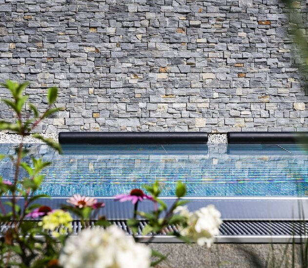 Pool mit Steinwand im Hintergrund und Blumen im Vordergrund