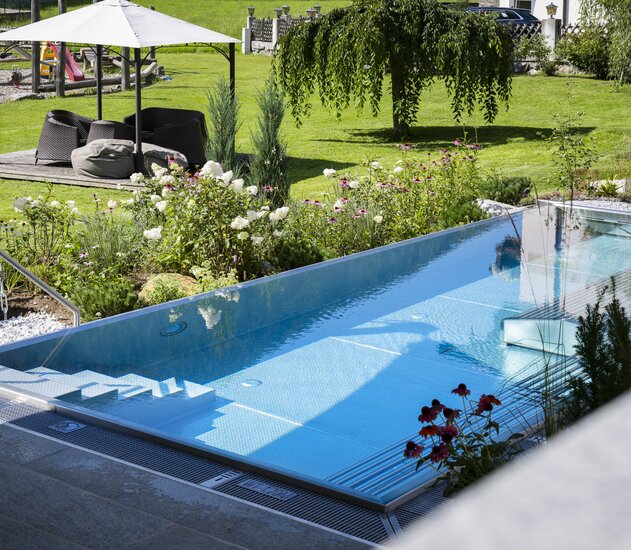 Rechteckiger Pool im Garten mit Liegebereich unter Sonnenschirm