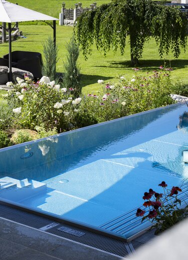 Rectangular pool in the garden with sunbathing area under parasol