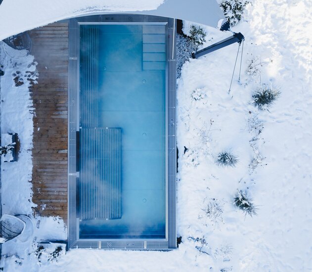 Draufsicht auf rechteckigen Pool im Schnee mit Rollladenabdeckung und angrenzendem Holzdeck