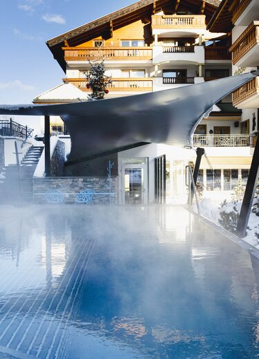 Winterlicher Außenpool mit Dampf vor Hotelgebäude