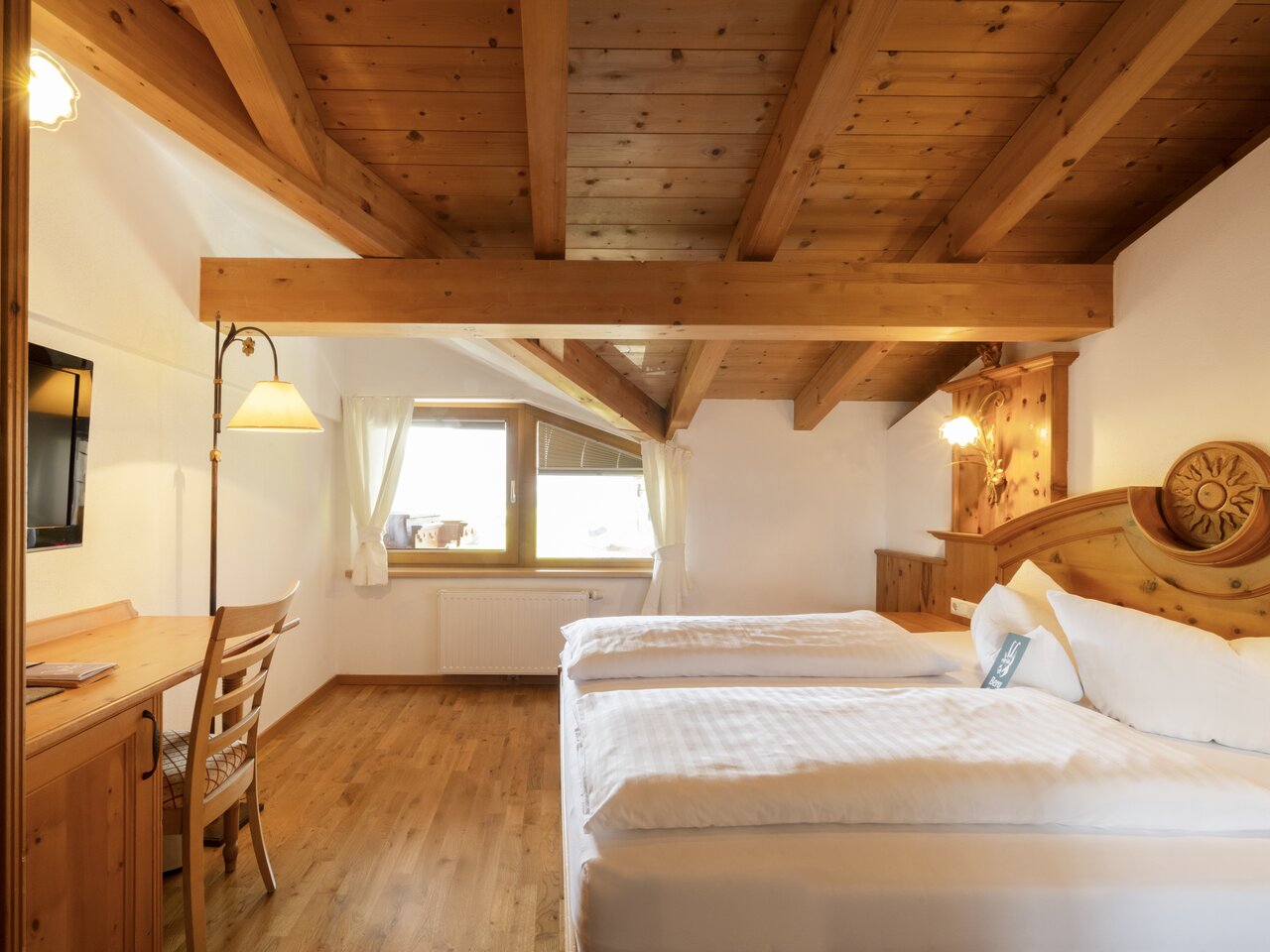 Schlafzimmer mit Dachschräge, Holzbalken, rotem Teppich und Vorhängen