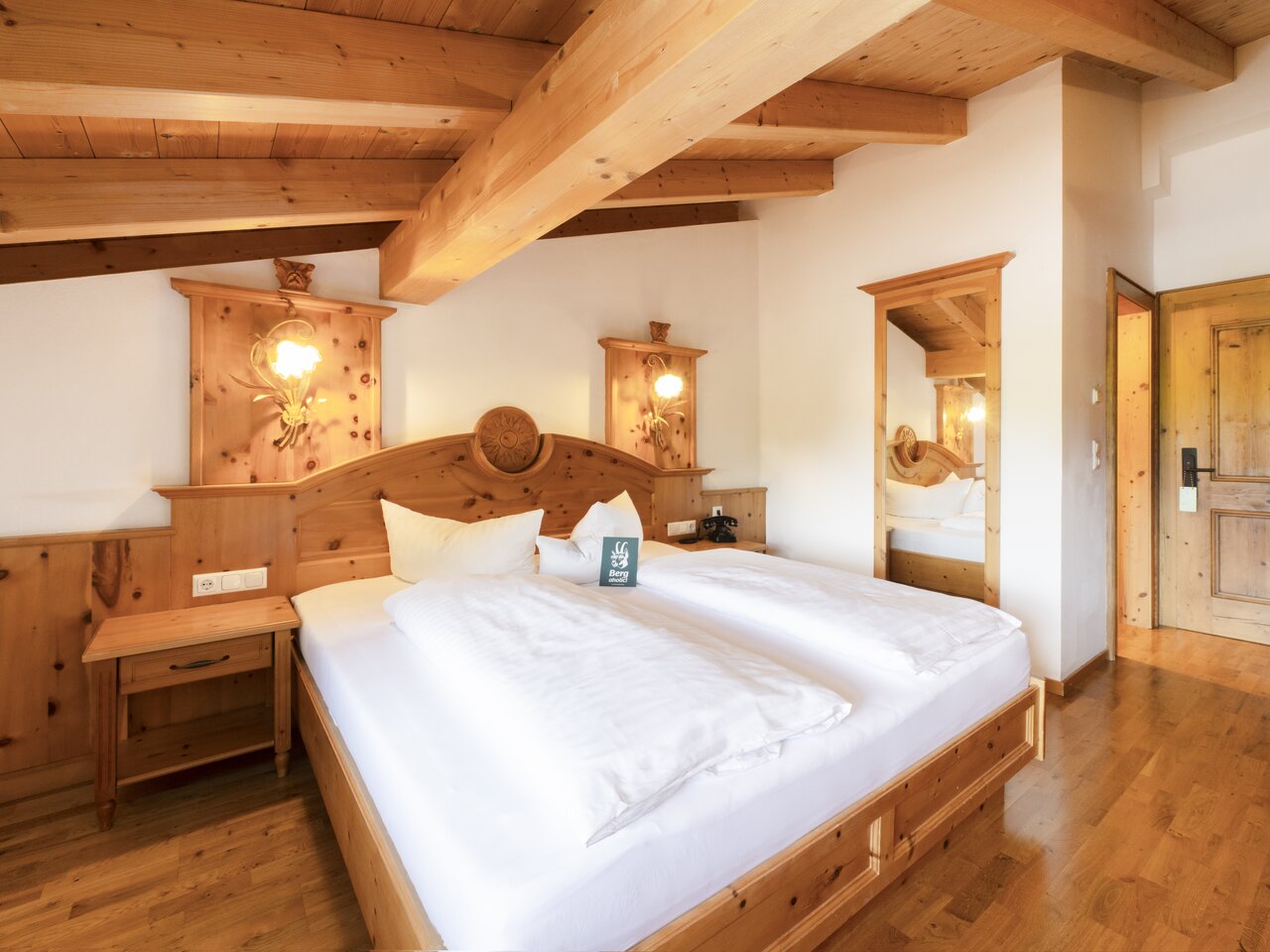 Hotelzimmer mit Holzbalkendecke, rotem Teppich und Bett
