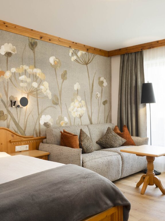 Gemütliches Hotelzimmer "Stubaier Zirbe" mit Bett, Sofa und floraler Tapete