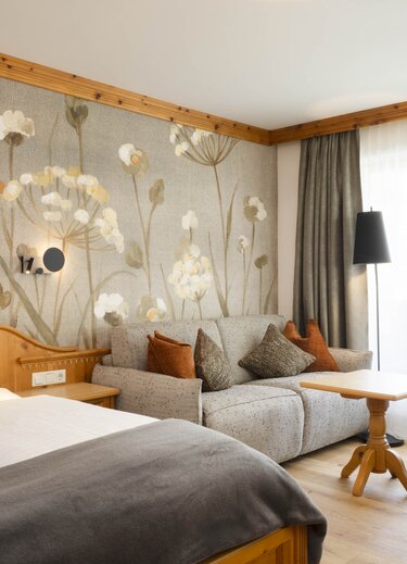 Gemütliches Hotelzimmer "Stubaier Zirbe" mit Bett, Sofa und floraler Tapete