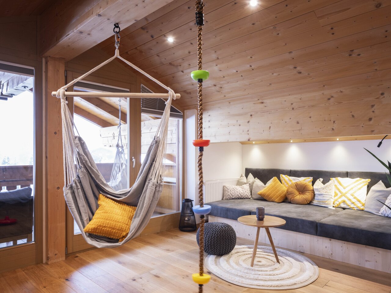 Hängesessel, Kletterseil und Sitzecke in einem hellen, holzvertäfelten Raum