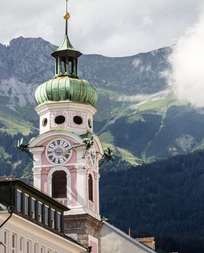Spitalskirche Innsbruck mit Kirchturm, Uhr und Bergen im Hintergrund