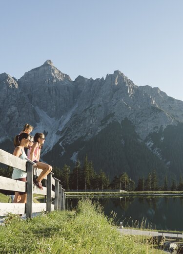 Familie sitzt auf Holzzaun am See vor Bergpanorama