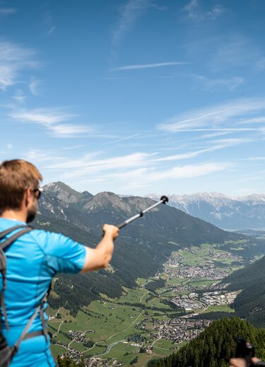 Wanderer zeigt mit Stock auf Tal in Berglandschaft unter blauem Himmel