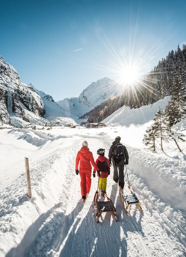 Familie zieht Schlitten durch verschneite Winterlandschaft im Stubaital, Sonnenschein