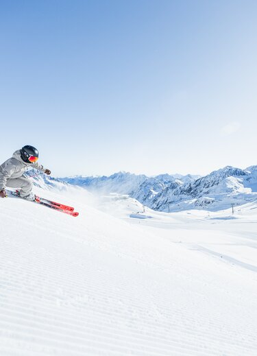 Dynamischer Skifahrer auf sonniger Skipiste vor Bergkette