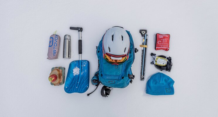 Ausrüstung für Skitouren auf Schnee: Rucksack, Helm, Schaufel, Sonde, Thermoskanne, Erste Hilfe Set